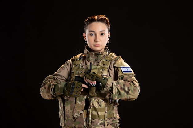 Femme soldat en camouflage visant le pistolet sur le mur noir