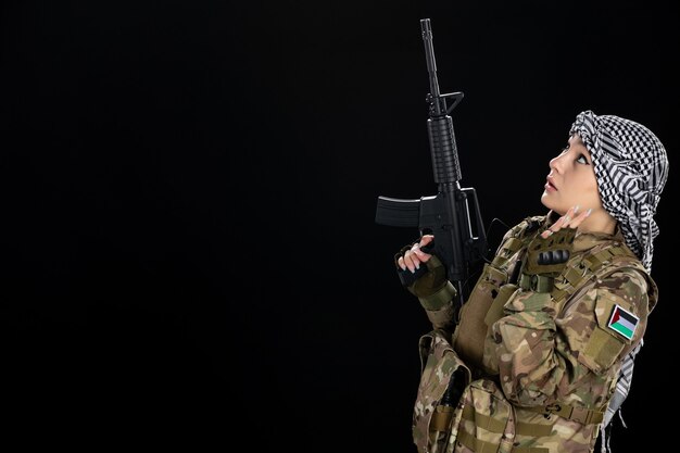 Femme soldat en uniforme militaire avec fusil sur le mur noir