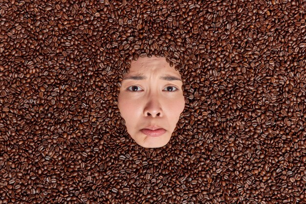 Une femme sombre et bouleversée ne montre que son visage à travers les grains de café