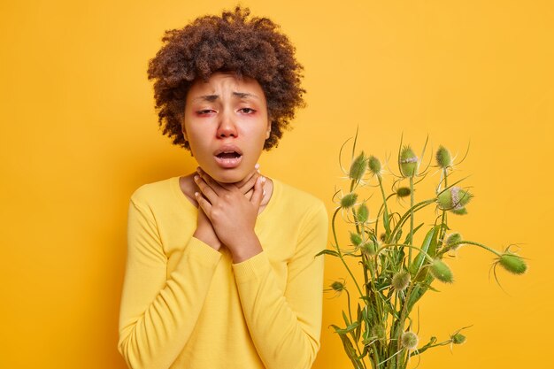 la femme souffre d'étouffement garde les mains sur le cou réagit sur la gâchette a les yeux rouges se sent malsaine vêtue d'un pull décontracté isolé sur jaune