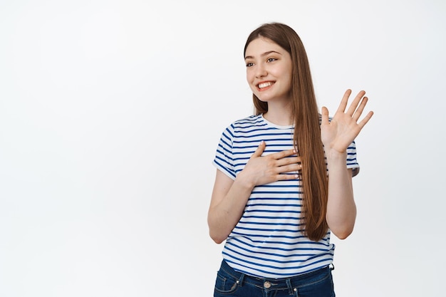 Femme souriante agitant sa main de côté et ayant l'air amicale, saluant quelqu'un, se présentant, debout sur fond blanc