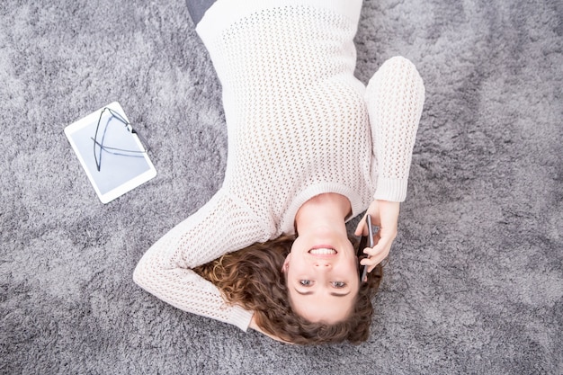 Femme souriante allongée sur le sol et appelant le téléphone