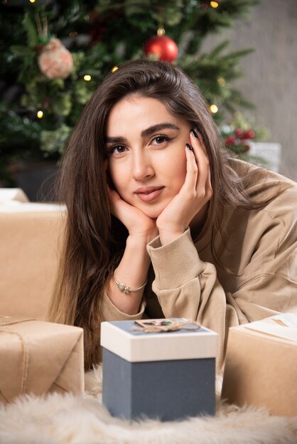 Femme souriante allongée sur un tapis moelleux avec des cadeaux de Noël.