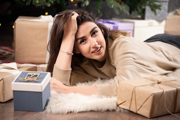 Femme souriante allongée sur un tapis moelleux avec des cadeaux de Noël.