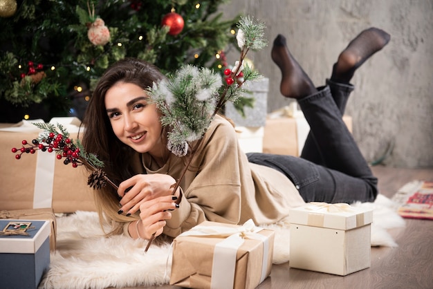Femme souriante allongée sur un tapis moelleux avec des cadeaux de Noël.