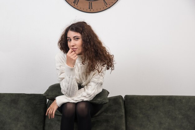 Une femme souriante assise sur un canapé et regardant la caméra