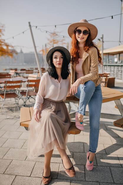 Femme souriante au gingembre en jeans assis sur une table dans un café en plein air