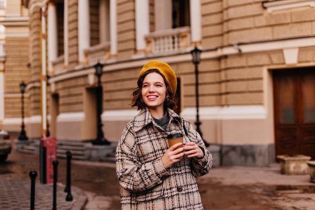 Femme souriante en béret jaune aime se promener dans la ville