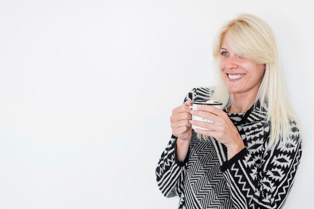 Femme souriante avec une boisson chaude en détournant les yeux