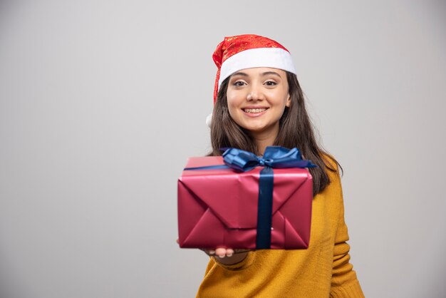 Femme souriante en bonnet de Noel montrant une boîte-cadeau.