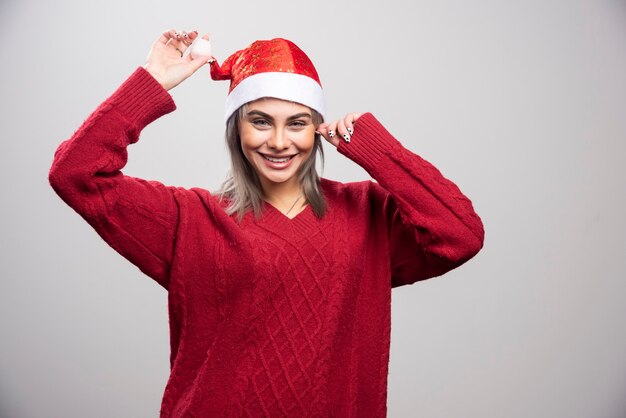 Femme souriante en bonnet de Noel posant sur fond gris.