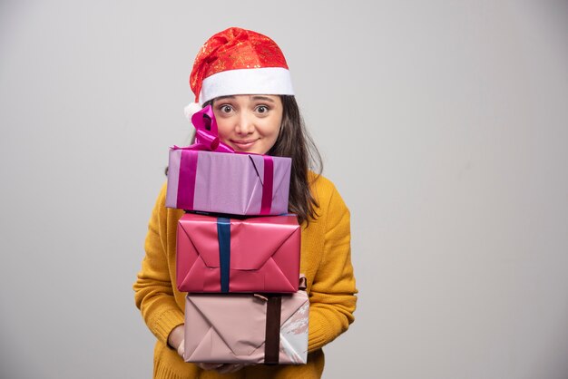 Femme souriante en bonnet de Noel tenant des coffrets cadeaux.