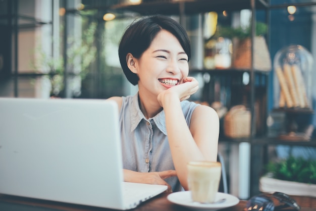 Femme souriante avec un café et un ordinateur portable