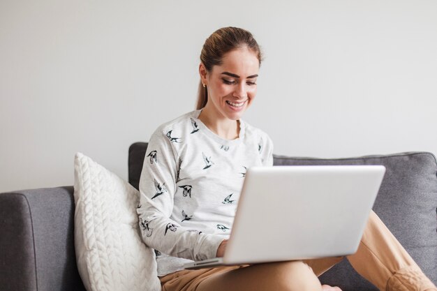 Femme souriante sur le canapé avec un ordinateur portable