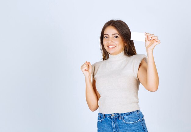 Femme souriante en chemise beige montrant sa carte sur fond blanc.