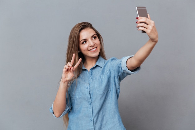 Femme souriante en chemise faisant selfie sur smartphone