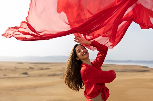 Femme souriante à coup moyen jetant une écharpe rouge