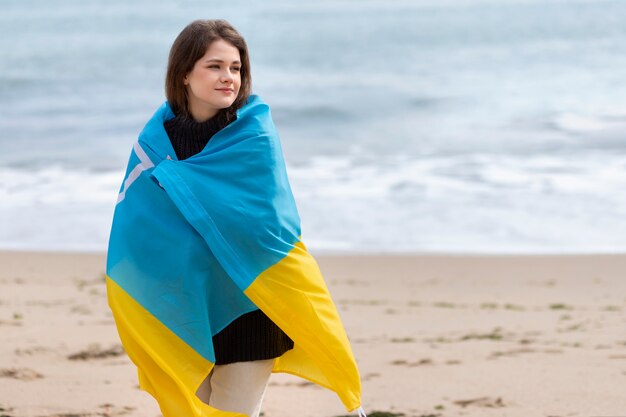 Femme souriante à coup moyen portant le drapeau ukrainien à la plage