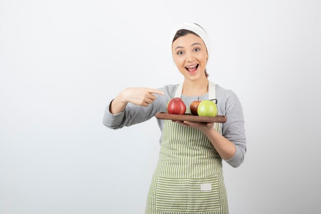 femme souriante cuisinier tenant une assiette de pommes sur blanc.