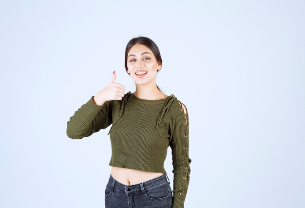 Femme souriante donnant les pouces vers le haut avec une expression heureuse sur fond blanc.