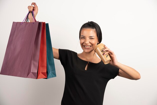 Femme souriante avec du café tenant des sacs à provisions.