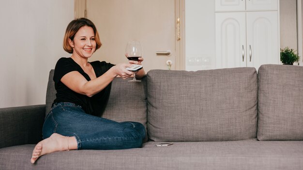 Femme souriante avec du vin et télécommande