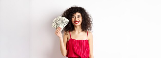 Femme souriante élégante en robe rouge montrant de l'argent debout sur fond blanc