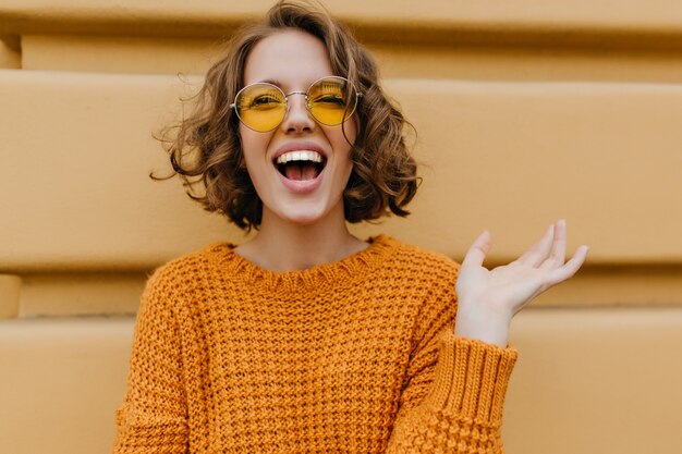 Femme souriante enthousiaste avec des boucles brillantes posant devant le vieux mur