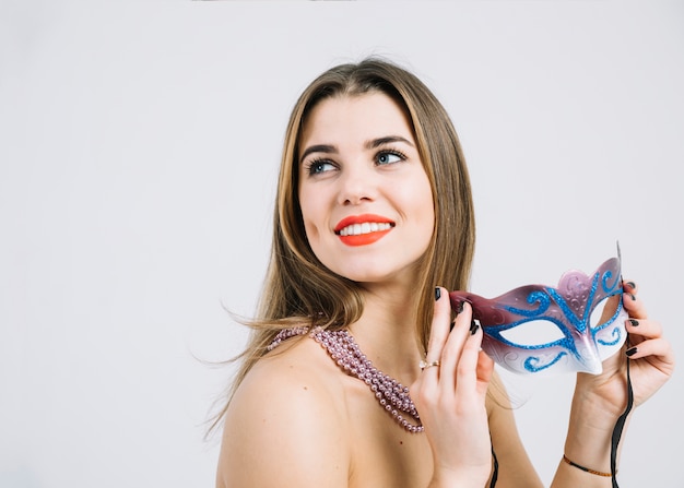 Femme souriante envisagée avec collier de perles tenant un masque de carnaval mascarade