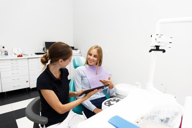 Femme souriante est assis sur la chaise au bureau de dentiste pendant que le médecin lui montre quelque chose