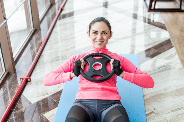 Photo gratuite femme souriante, exercant des abdos avec une plaque de poids