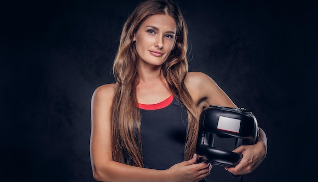 Une femme souriante et heureuse portant des gants de boxeur tient un casque de protection au studio.