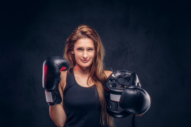 Une femme souriante et heureuse portant des gants de boxeur tient un casque de protection au studio.