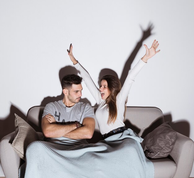 Femme souriante et homme en colère devant la télé sur un canapé