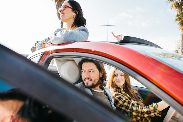 Femme souriante et homme positif assis dans la voiture près de Dame se penchant de l'auto