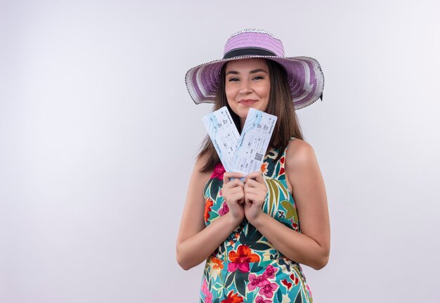 Femme souriante jeune voyageur portant une robe multicolore au chapeau tenant un billet sur un mur blanc