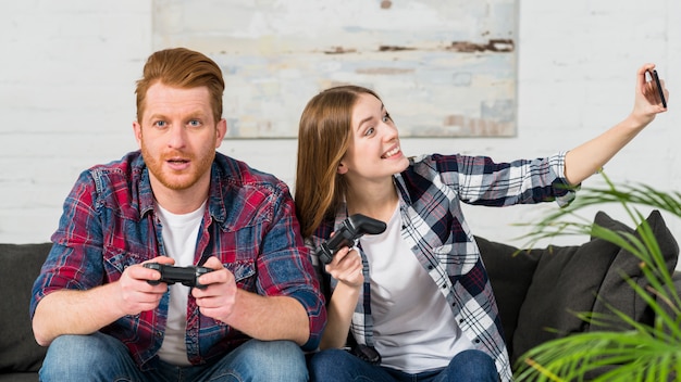 Photo gratuite femme souriante jouant à un jeu vidéo avec son petit ami prenant selfie sur smartphone
