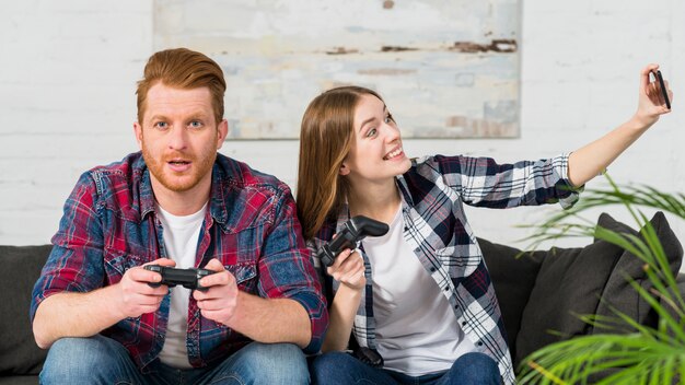 Femme souriante jouant à un jeu vidéo avec son petit ami prenant selfie sur smartphone