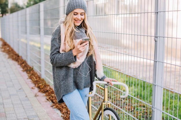 Femme souriante, marchant avec smartphone et vélo