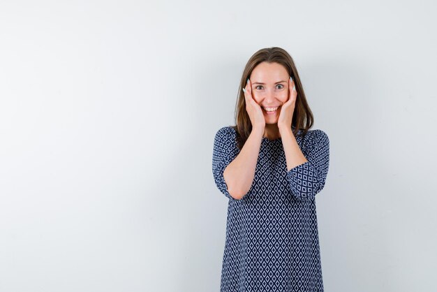 La femme souriante met ses mains sur les joues sur fond blanc