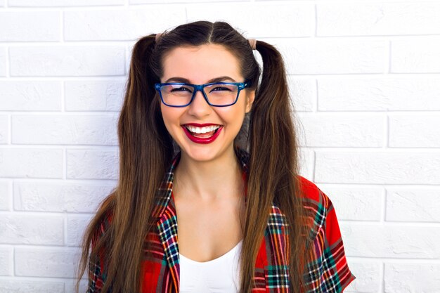 Femme souriante mignonne drôle. Belle femme jolie hipster en riant avec de longs poils brune étonnante et un maquillage lumineux. portant des lunettes et une chemise à carreaux.