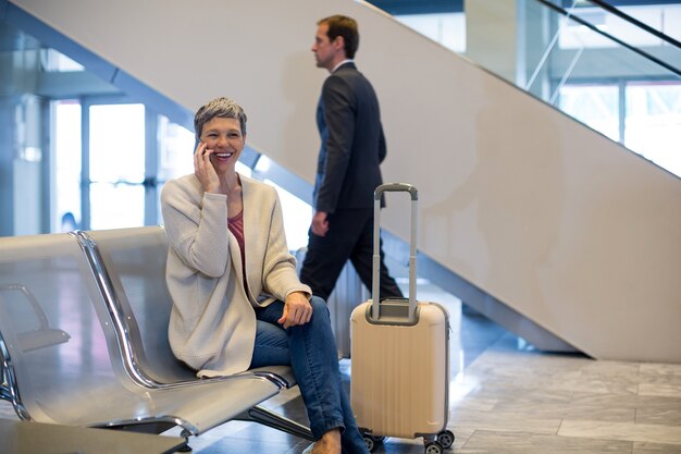 Femme souriante parlant au téléphone mobile dans la zone d'attente