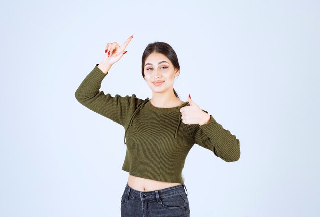 Une femme souriante pointant vers le haut avec un index et montrant un pouce vers le haut.