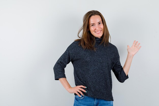 La femme souriante pointe vers la droite avec la main et met l'autre main sur la taille sur fond blanc