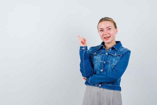 La femme souriante pointe vers le haut avec son index sur fond blanc