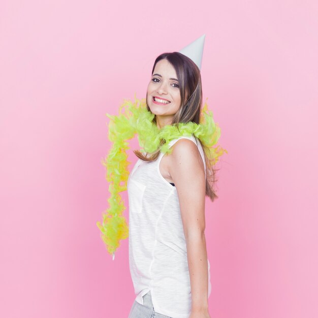 Femme souriante, portant le boa de plumes vertes autour de son cou et chapeau de fête contre la toile de fond rose