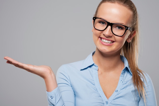 Femme souriante portant des lunettes de mode présentant quelque chose sur l'espace de copie