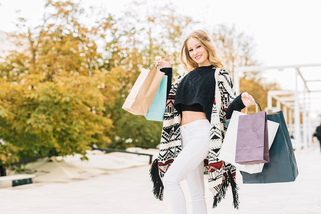 Photo gratuite femme souriante posant avec des sacs en papier dans le parc