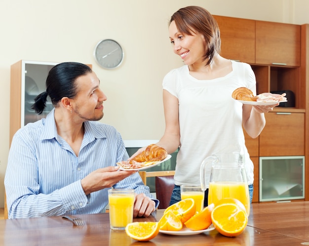 La femme souriante sert des croissants et des œufs brouillés son homme