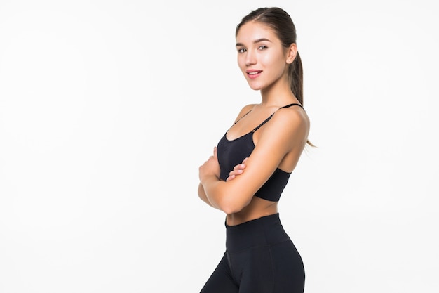 Femme souriante de sport debout avec les bras croisés et regardant la caméra isolée sur mur blanc